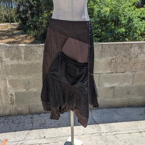 Puede incluir: Una falda asimétrica marrón y negra con un gran bolsillo en la parte delantera. La falda está hecha de una tela suave y fluida y tiene un ajuste holgado.