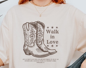 May include: A beige t-shirt with a graphic of two brown cowboy boots and the text "*** Walk in Love ***"  Just as Christ also loved you and gave himself up for us, an offering and a sacrifice to God as a fragrant aroma. Ephesians 5:2