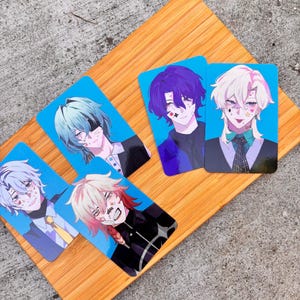 以下が含まれることがあります： カラフルな髪と顔のマークを持つ若い人々の、アニメスタイルのイラストが特徴の5枚のキャラクターアートカード。各カードは青色の背景で、木製の表面に表示されています。