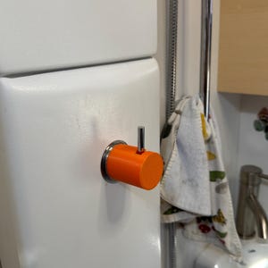 May include: A bright orange plastic hook with a silver metal hook attached to a white wall.