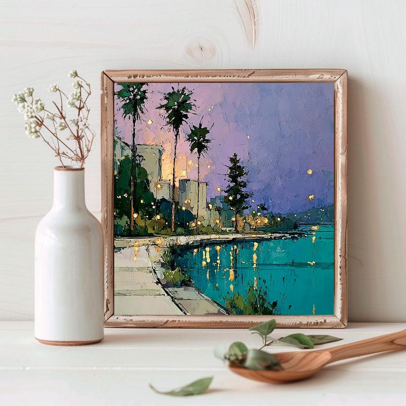 May include: Square framed painting of a coastal city scene. The artwork depicts palm trees, buildings, and a body of water under a purple and blue sky. The painting is in a wooden frame and is displayed on a white surface.