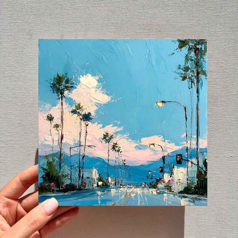 May include: An oil painting on canvas depicting a street scene with tall palm trees under a bright blue sky. The artwork features thick, textured brushstrokes in shades of blue, white, and soft pink, capturing a sunny day with light clouds.