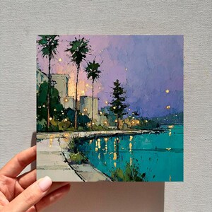 May include: An impressionistic painting of a waterfront scene at dusk. The artwork features palm trees, city buildings, and a teal-colored body of water reflecting lights. The sky transitions from purple to blue, creating a serene atmosphere.