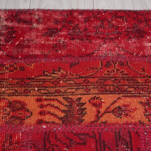 K&ouml;nnte beinhalten: Ein roter, orangefarbener und brauner Patchwork-Teppich mit einem Blumenmuster. Der Teppich ist aus Wolle und hat einen abgenutzten Look.