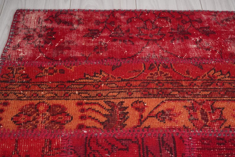 K&ouml;nnte beinhalten: Ein roter, orangefarbener und brauner Patchwork-Teppich mit einem Blumenmuster. Der Teppich ist aus Wolle und hat einen abgenutzten Look.