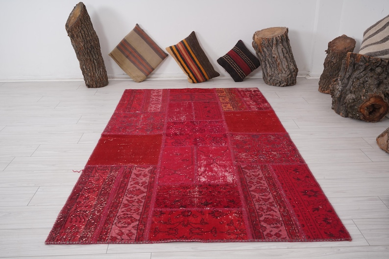 K&ouml;nnte beinhalten: Ein roter Patchwork-Teppich mit verschiedenen Mustern und Texturen. Der Teppich ist aus recycelten Materialien hergestellt und hat ein einzigartiges, handgemachtes Aussehen.