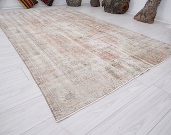 Op de afbeelding: Een vintage tapijt met een vervaagd bloemenpatroon in beige, bruin en roze tinten. Het tapijt heeft een verweerde uitstraling en een versleten rand.