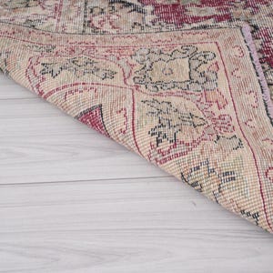 May include: Close-up of the edge of a vintage rug with a floral pattern in shades of pink, red, and cream. The rug has a frayed edge and is woven with a fine texture.