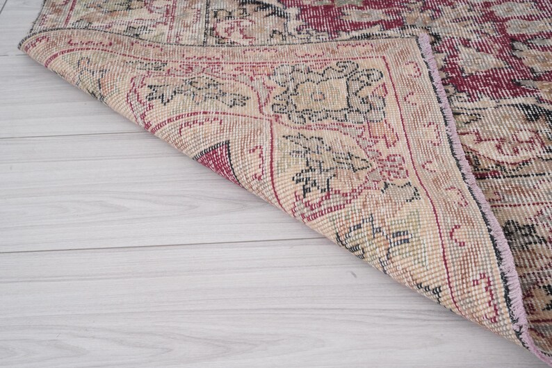 May include: Close-up of the edge of a vintage rug with a floral pattern in shades of pink, red, and cream. The rug has a frayed edge and is woven with a fine texture.