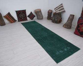 May include: A long, rectangular, emerald green rug. The rug is placed on a light-colored wooden floor. Decorative pillows and wooden tree trunk sections are arranged around the rug.