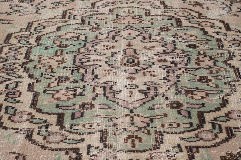 May include: Close-up of a vintage rug with a detailed, symmetrical pattern. The rug features a central medallion design in shades of green, brown, and beige, with intricate floral and geometric motifs. The rug has a distressed, antique appearance.