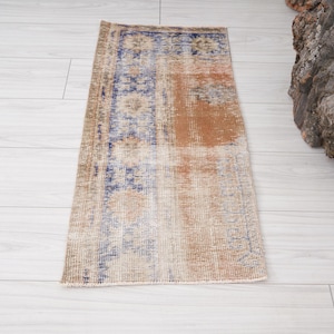 May include: Rectangular vintage rug with a distressed design. The rug features a central section with a faded orange hue, bordered by a blue and beige patterned section. The rug is placed on a light wood floor.
