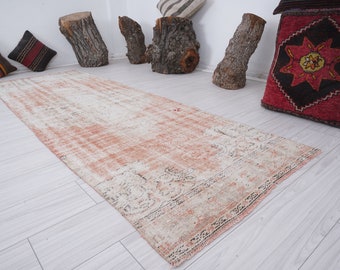 May include: A vintage, off-white and peach-colored rug with a faded floral pattern. The rug is laid out on a light wood floor.
