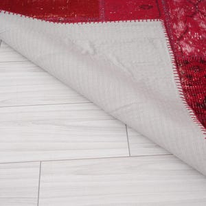 K&ouml;nnte beinhalten: Ein roter und wei&szlig;er Patchwork-Teppich mit einer wei&szlig;en R&uuml;ckseite. Der Teppich ist in der Mitte gefaltet und die R&uuml;ckseite ist sichtbar.