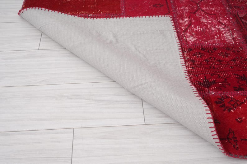 K&ouml;nnte beinhalten: Ein roter und wei&szlig;er Patchwork-Teppich mit einer wei&szlig;en R&uuml;ckseite. Der Teppich ist in der Mitte gefaltet und die R&uuml;ckseite ist sichtbar.