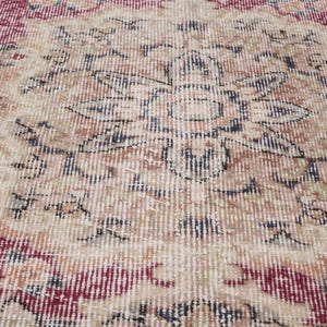 May include: Close-up of a vintage rug with a floral pattern in shades of red, beige, and black. The rug has a distressed look, with faded colors and a worn texture.