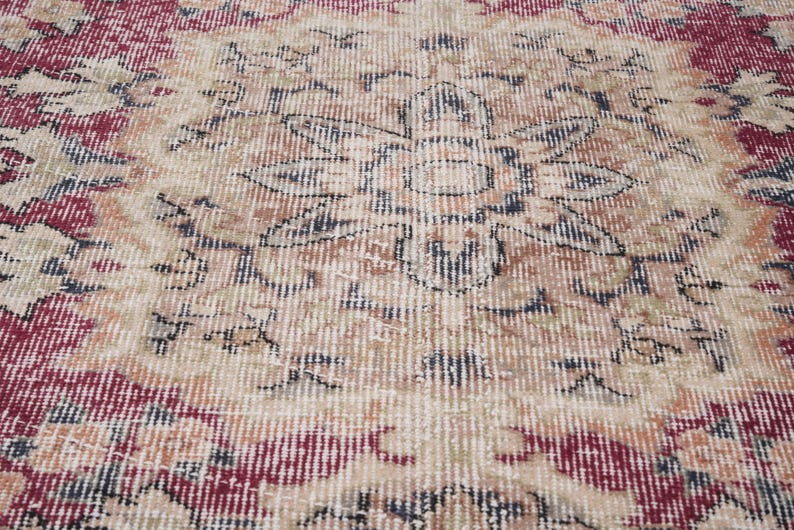 May include: Close-up of a vintage rug with a floral pattern in shades of red, beige, and black. The rug has a distressed look, with faded colors and a worn texture.