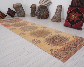 Op de afbeelding: Een vintage loper met een beige achtergrond en ingewikkelde bloemmotieven in tinten bruin, rood en groen. De loper heeft een verweerde uitstraling en is perfect om een ​​bohemien touch aan elke kamer toe te voegen.