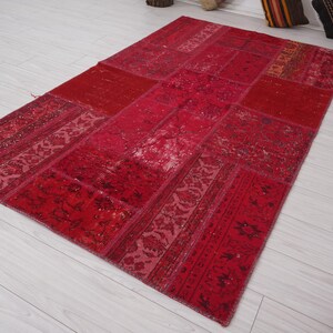 K&ouml;nnte beinhalten: Ein roter Patchwork-Teppich mit verschiedenen Mustern und Texturen. Der Teppich ist aus recycelten Materialien hergestellt und hat einen einzigartigen, handgefertigten Look.
