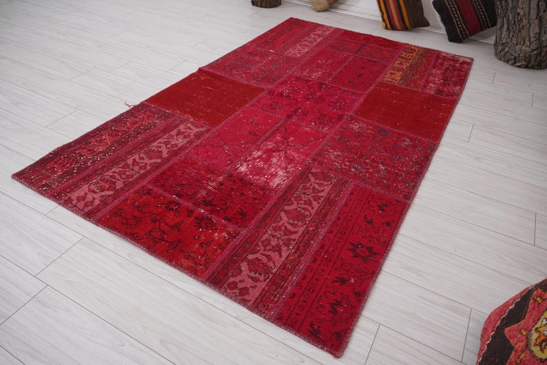 K&ouml;nnte beinhalten: Ein roter Patchwork-Teppich mit verschiedenen Mustern und Texturen. Der Teppich ist aus recycelten Materialien hergestellt und hat einen einzigartigen, handgefertigten Look.