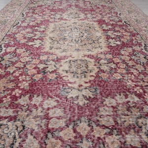 May include: A vintage rug with a faded red, cream, and black floral pattern. The rug has a distressed look and is made of a woven material.