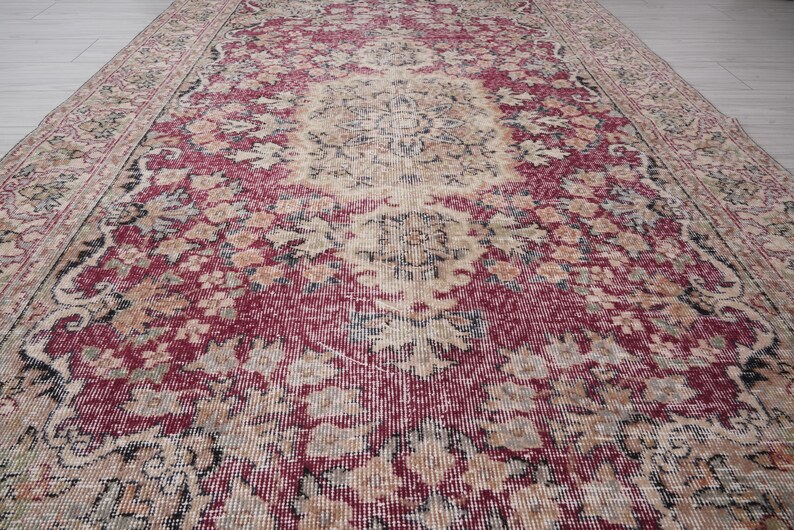 May include: A vintage rug with a faded red, cream, and black floral pattern. The rug has a distressed look and is made of a woven material.