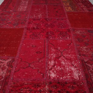 K&ouml;nnte beinhalten: Ein roter Patchwork-Teppich mit verschiedenen Mustern und Texturen. Der Teppich ist aus recycelten Materialien hergestellt und hat einen Vintage-Look.