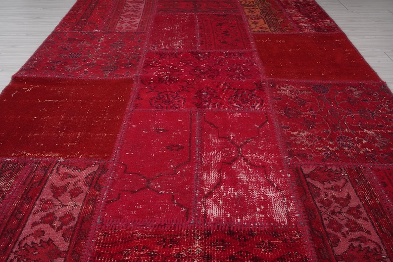K&ouml;nnte beinhalten: Ein roter Patchwork-Teppich mit verschiedenen Mustern und Texturen. Der Teppich ist aus recycelten Materialien hergestellt und hat einen Vintage-Look.