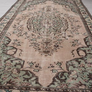 May include: A rectangular, vintage rug with a central medallion design. The rug features a faded colour palette of blush pink, sage green, and brown, with intricate floral and geometric patterns. The border is a darker brown with repeating floral motifs.