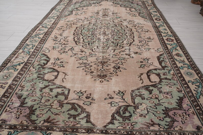 May include: A rectangular, vintage rug with a central medallion design. The rug features a faded colour palette of blush pink, sage green, and brown, with intricate floral and geometric patterns. The border is a darker brown with repeating floral motifs.