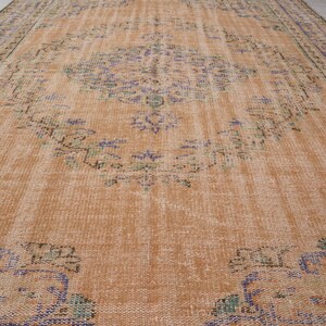 Pu&ograve; includere: Un grande tappeto vintage rettangolare dall'aspetto invecchiato. Il tappeto presenta un colore di base marrone-arancio caldo con motivi floreali e geometrici sbiaditi nelle tonalit&agrave; del blu, verde e viola. I bordi hanno un bordo pi&ugrave; scuro.