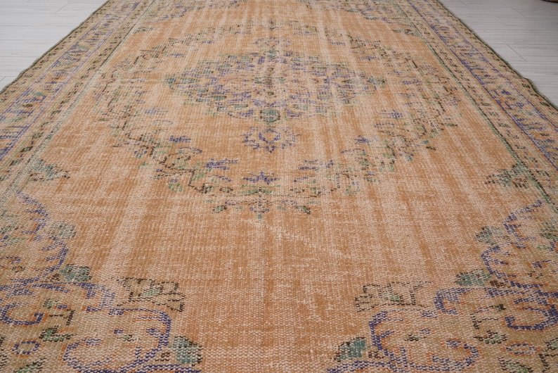 Pu&ograve; includere: Un grande tappeto vintage rettangolare dall'aspetto invecchiato. Il tappeto presenta un colore di base marrone-arancio caldo con motivi floreali e geometrici sbiaditi nelle tonalit&agrave; del blu, verde e viola. I bordi hanno un bordo pi&ugrave; scuro.
