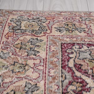 May include: A beige rug with a red and gray floral pattern. The rug has a border with a repeating pattern of leaves and flowers.
