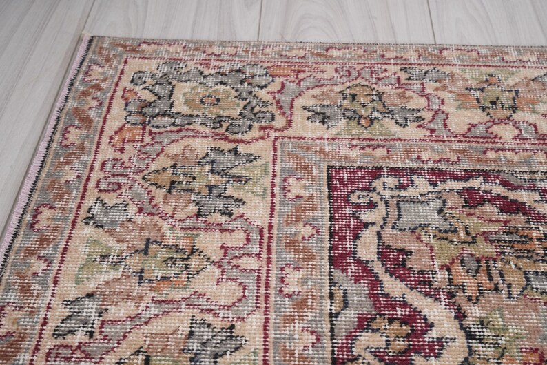 May include: A beige rug with a red and gray floral pattern. The rug has a border with a repeating pattern of leaves and flowers.
