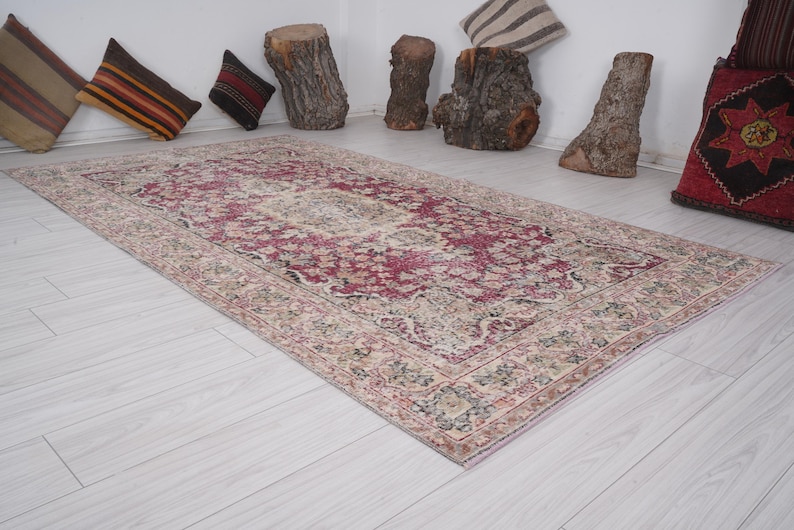 May include: A vintage rug with a pink and cream floral pattern. The rug has a distressed look and is perfect for adding a touch of bohemian style to any room.