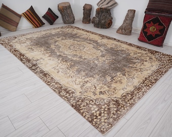 May include: A rectangular, vintage-style rug with a central medallion design in shades of beige and brown. The rug features a detailed floral pattern and a dark brown border. Decorative pillows and wood accents are in the background.