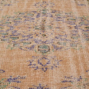 Pu&ograve; includere: Primo piano di un tappeto vintage dall'aspetto usurato e sbiadito. Il tappeto presenta un motivo a medaglione centrale nei toni del blu, verde e marrone su uno sfondo beige. Il motivo &egrave; intricato e dettagliato, con usura visibile.