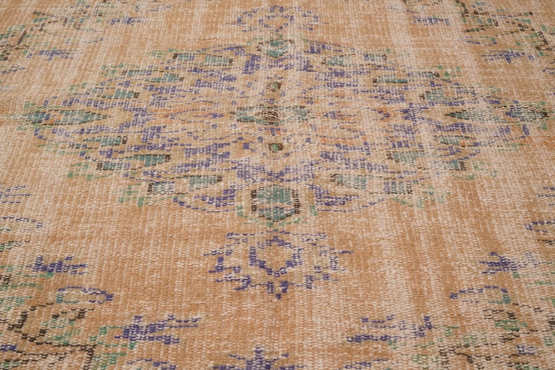 Pu&ograve; includere: Primo piano di un tappeto vintage dall'aspetto usurato e sbiadito. Il tappeto presenta un motivo a medaglione centrale nei toni del blu, verde e marrone su uno sfondo beige. Il motivo &egrave; intricato e dettagliato, con usura visibile.
