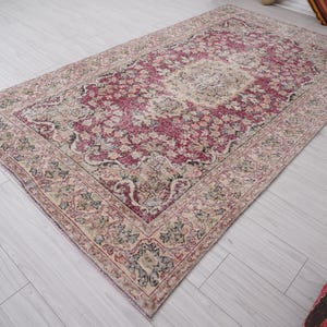 May include: A vintage rug with a faded pink and cream floral pattern. The rug has a distressed look with a worn and faded appearance.