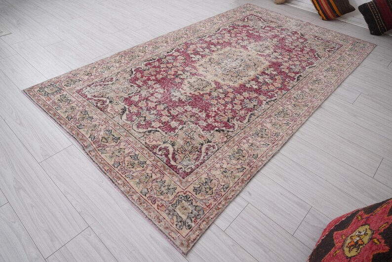 May include: A vintage rug with a faded pink and cream floral pattern. The rug has a distressed look with a worn and faded appearance.