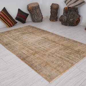 Può includere: Un tappeto vintage color marrone chiaro con un motivo sbiadito. Il tappeto è steso su un pavimento in legno bianco.