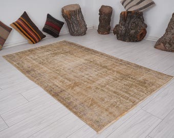 May include: A light brown vintage rug with a faded pattern. The rug is laid out on a white wood floor.