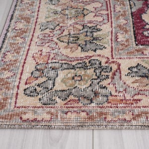 May include: Close-up of the edge of a beige rug with a floral pattern. The rug has a burgundy border and intricate details in shades of brown, gray, and black.