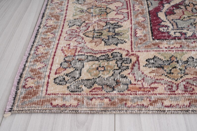 May include: Close-up of the edge of a beige rug with a floral pattern. The rug has a burgundy border and intricate details in shades of brown, gray, and black.
