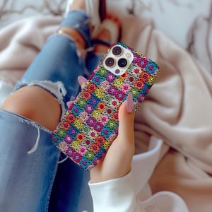 May include: A colorful phone case with a crocheted pattern in shades of pink, blue, green, and yellow. The case has a raised camera bump and a white background.