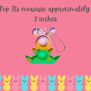 May include: A colorful pop it toy shaped like a bunny with a green, yellow, and blue design. The toy is approximately 2 inches tall and has a string attached to it. The toy is surrounded by a row of pastel pink, yellow, and blue bunny-shaped candies.
