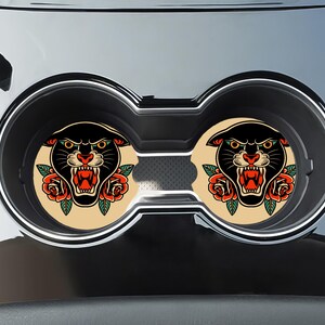 May include: Two black panther head car coasters with red roses and a vintage tattoo style. The coasters are beige with a black outline.