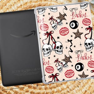 May include: Black e-reader with a decorative case. The case features a light pink background with a pattern of skulls, stars, lips, and the word "Lucky". The skulls have red bows, and the stars have a leopard print.