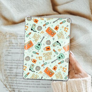 May include: A light green tablet case with a repeating pattern of musical instruments, cowboy boots, disco balls, and the words "SHOW GIRL" and the number "12". The case is held in a person's hand.