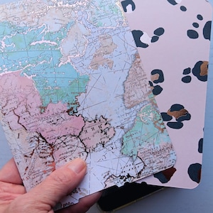 May include: Two decorative tags. One tag features a vintage world map design with pastel colors and gold accents. The other tag has a pink background with black and gold leopard print spots. Both tags have a rounded top edge.